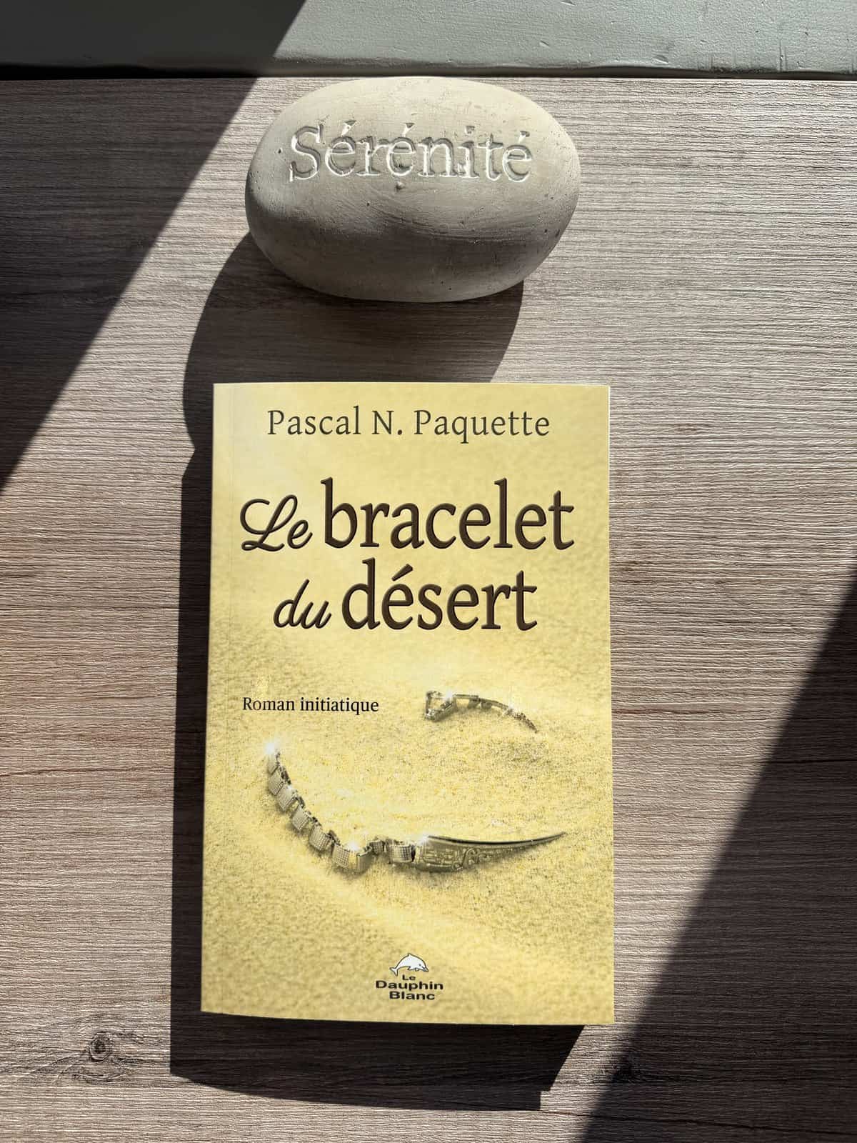 Le roman Le Bracelet du Désert de Pascal N.&nbsp;Paquette, posé sur une table de bois près d'une pierre gravée Sérénité