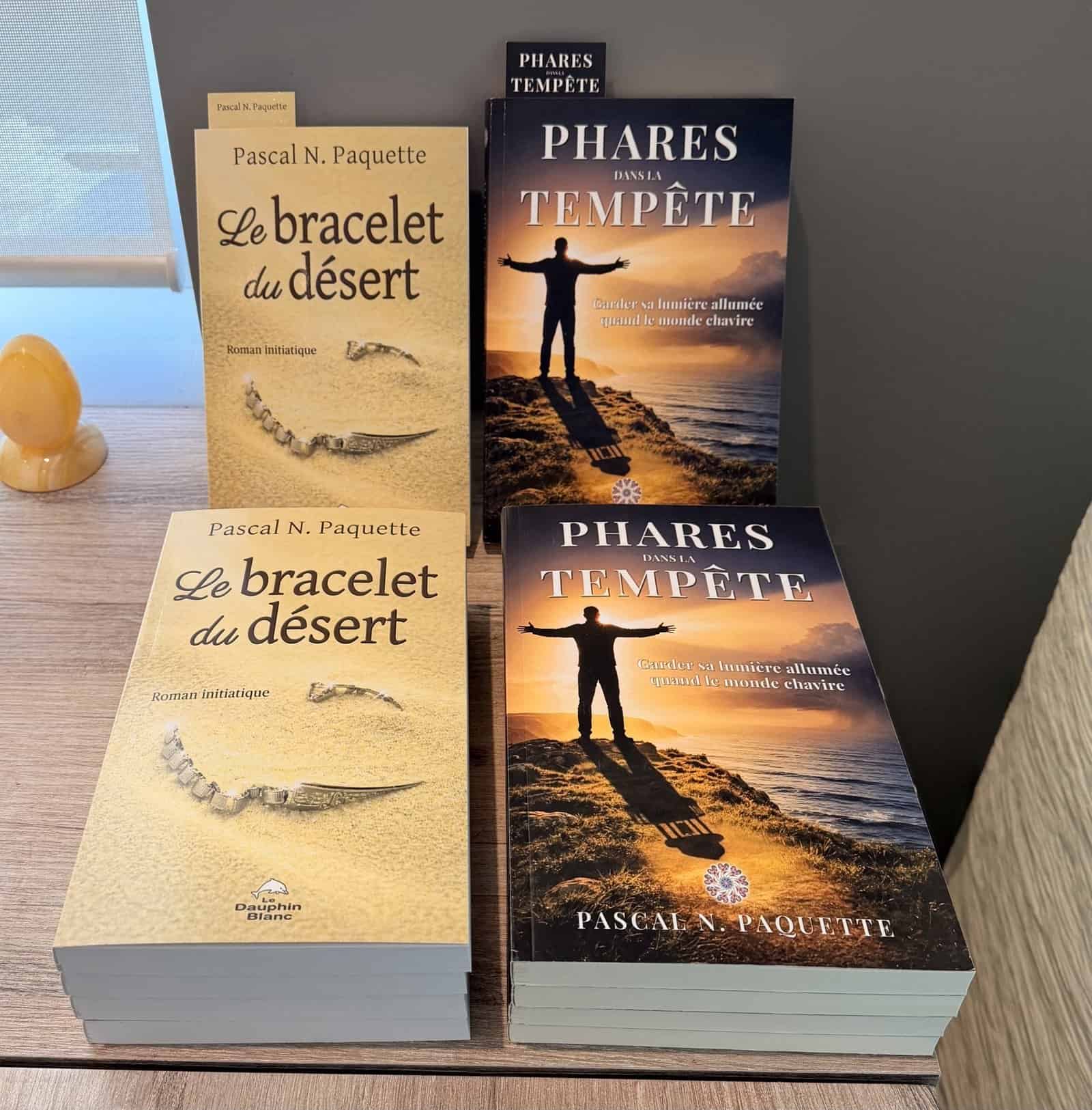 Les livres Le Bracelet du Désert et Phares dans la Tempête de Pascal N. Paquette, en piles sur un meuble de bois