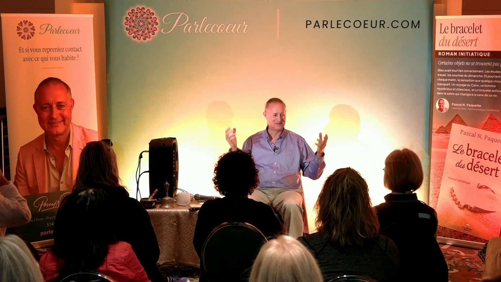 Pascal N. Paquette en conférence devant la bannière Parlecoeur, les bras levés, face à la salle