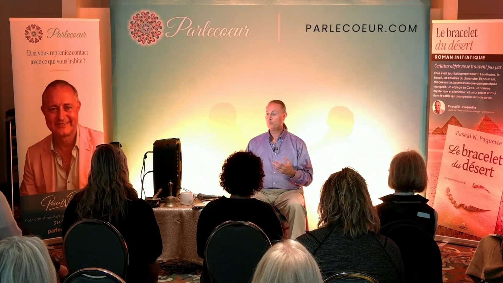 Pascal N. Paquette speaking, seen from the audience, in front of the Parlecoeur banner